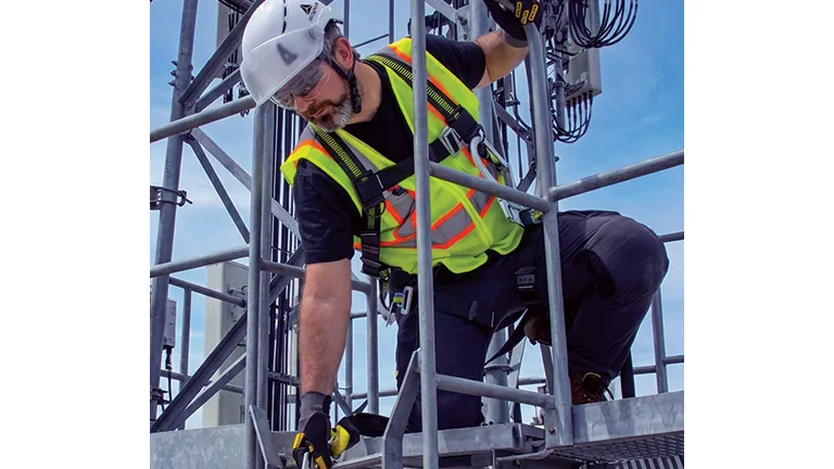 Worker on scaffolding wearing a high-visibility harness and fall-protection equipment.